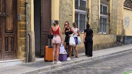 Cuatro chicas con maletas llegan a una finca en una calle del centro de Cádiz, símbolo del impacto del alquiler vacacional sobre el acceso a la vivienda.