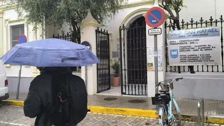 Entrada del CEIP San Rafael con una persona pasando con paraguas por delante.