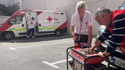 Ambulancia de la Cruz Roja al fondo y en primer término dos personas de Cruz Roja junto a un generador eléctrico.