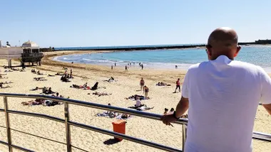 Un hombre observa la playa de la Caleta con numerosas personas tomando el sol en la tarde de este 22 de abril.