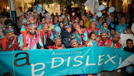 Personas vestidas con disfraces tras una pancarta en color turquesa de ADICA.