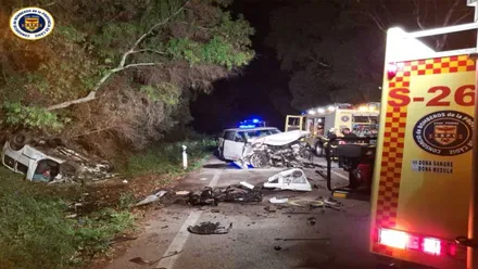 Dos coches accidentados destrozados, en color blanco, a la izquierda el camión de bomberos con luces rojas iluminadas.