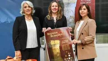 El cartel de la XVI Bajada Romana en manos de Vanesa Beltrán, Patricia Caro y Josefina Herrera. El cartel destaca por sus tonos marrones y amarillos.