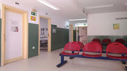 Sala de espera de un ambulatorio con asientos rojos, pared blanca y verde y puertas en tono blanco con marco beige.