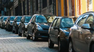 Fila de coches aparcados en una calle, casi todos en tonos oscuros.