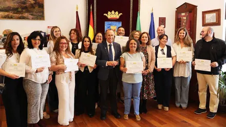 Los alumnos y alumnas del curso, en pie, junto al alcalde, muestran el sus manos el diploma acreditativo. De fondo el salón municipal.