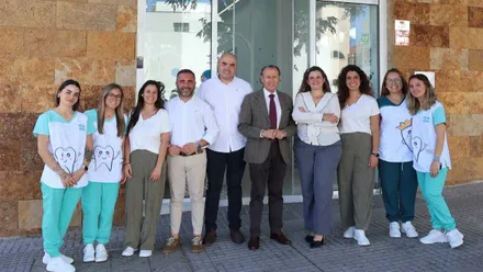 Alcalde y empleados delante de la fachada del Centro Dental Infantil Ávila Bobillo, destacan los tonos tierra y la indumentaria blanca y verde de los empleados.