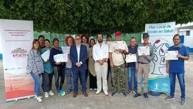 Grupo de personas en un jardín con sus diplomas en la mano y varios carteles del programa Eracis+ a derecha e izquierda.