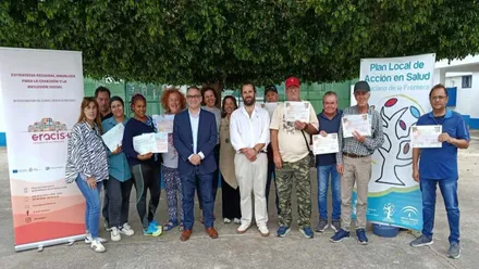 Grupo de personas en un jardín con sus diplomas en la mano y varios carteles del programa Eracis+ a derecha e izquierda.