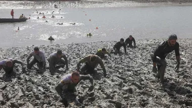 Corredores nadando y avanzando entre el barro de la prueba deportiva.
