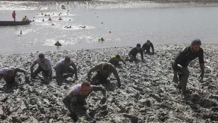 Corredores nadando y avanzando entre el barro de la prueba deportiva.