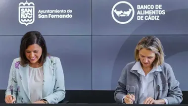 Patricia Cavada e Isabel Gomis en la firma del acuerdo entre el ayuntamiento de San Fernando y el Banco de Alimentos, tras ellas una pantalla en tonos grises.