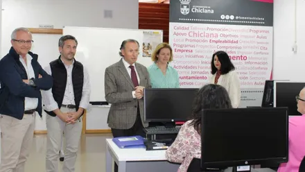 En un aula de formación, con personas y ordenadores, con fondo de pizarras y pared blanca, el alcalde José María Román y otras personas.