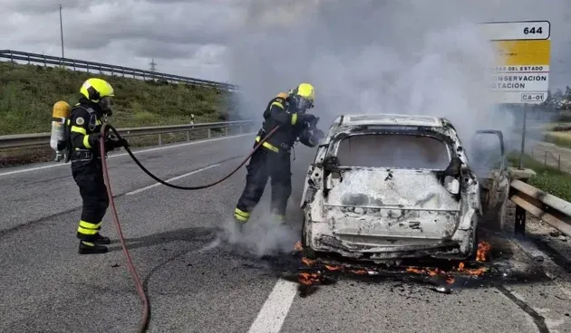 Vehículo ardiendo en la A4 mientras dos bomberos intentan apagar el fuego.