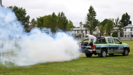 Vehículo verde y negro sobre el césped soltando producto contra los mosquitos.