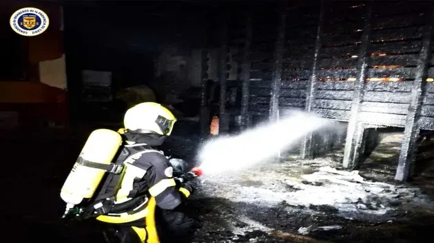 Bombero dirigiendo un chorro de agua hacia el foco carbonizado del incendio, viste de negro con un extintor color amarillento.