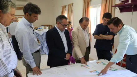 José María Román con chaqueta blanca, alcalde de Chiclana, mirando unos planos en una mesa y rodeado de otras personas.