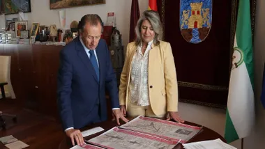 El alcalde junto a la delegada de Chiclana mirando un plano sobre una mesa y la bandera andaluza a un lado.