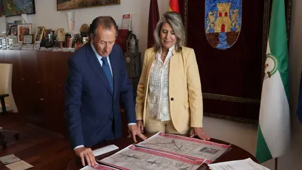 El alcalde junto a la delegada de Chiclana mirando un plano sobre una mesa y la bandera andaluza a un lado.