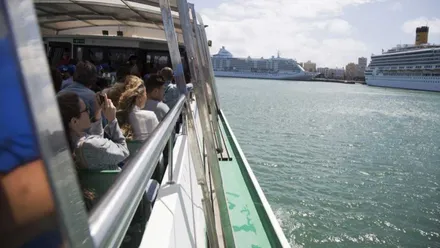 Personas en un barco visitando el puerto de Cádiz, a la derecha un buque de pasajeros.
