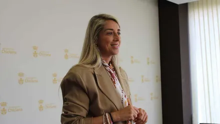 Isabel Butrón, delegada de Hacienda en Chiclana, con chaqueta beige y, tras ella, un panel blanco con el escudo de Chiclana en dorado.