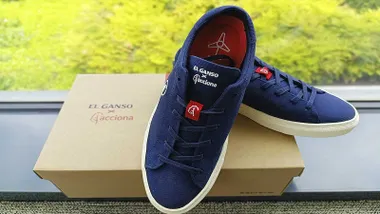 un par de zapatillas recicladas de palas, en color azul, sobre una caja de cartón y fondo natural verde.