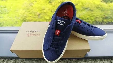 un par de zapatillas recicladas de palas, en color azul, sobre una caja de cartón y fondo natural verde.