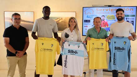 Organizadores del Campus en Chiclana con dos jugadores del Cádiz sosteniendo las camisetas en sus manos destacando el color amarillo y celeste o blanco.