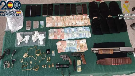 Billetes, armas y droga incautadas por la Policía Nacional y la Guardia Civil expuestos sobre mesa con tapiz verde.