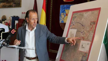 José María Román, de chaqueta gris, indica sobre un panel y un mapa la ubicación geográfica del depósito.