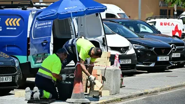 Dos operarios se protegen del sol con una sombrilla mientras trabajan en la calle