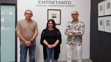 Susana Rivas con el autor posando junto a una de las obras, en pared blanca, de "Entretanto".