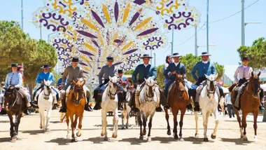 Jinetes pasando por los arcos de luz, amarillas y moradas, de la Feria de Chiclana.