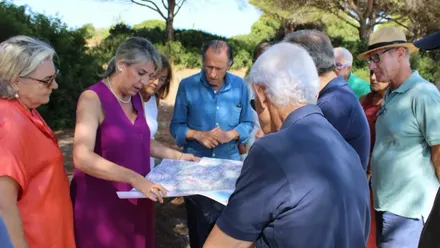 El alcalde obser va un plano rodeado de vecinos, lleva una camisa azul.