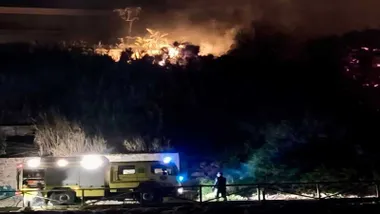Camión de bomberos y a lo lejos el foco del incendio destacando en tonos amarillos.