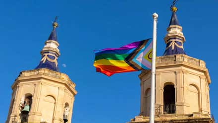 Bandera arco iris del colectivo LGTBIQ+ en el izado, tras ella las dos torres de la plaza.