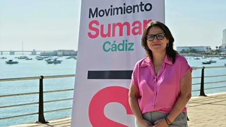 Esther Gil, con camisa rosa, junto a un cartel de Sumar y de fondo el mar.