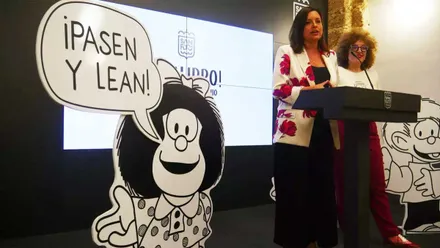 Patricia Cavada presentando el acto en el atril junto a una caricatura de Mafalda en Blanco y Negro.