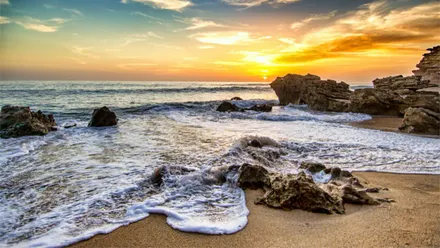 El sol se va poniendo con la orilla de esta playa de Cádiz con rocas en primer plano