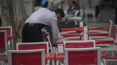 Camarero limpiando sillas rojas en una terraza.