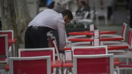 Camarero limpiando sillas rojas en una terraza.