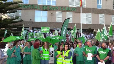 Personal, vistiendo de verde, manifestándose con banderas y paraguas, a puertas del hospital San Carlos.