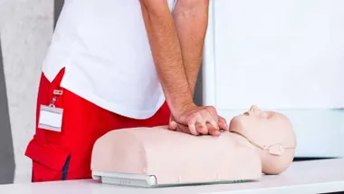 Realización de una RCP a un muñeco, lo hace un experto con pantalón rojo y chaleco blanco.