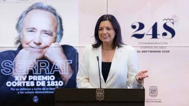 Patricia Cavada con chaqueta blanca y a su espalda, en una pantalla, la imagen de Joan Manuel Serrat.