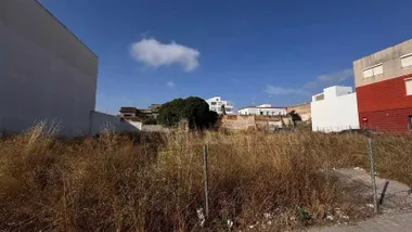 Estado del solar del mercado con vegetación seca, valla y mal estado.