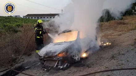 Bombero vestido de azul y casco amarillo apaga el incendio en el coche calcinado.