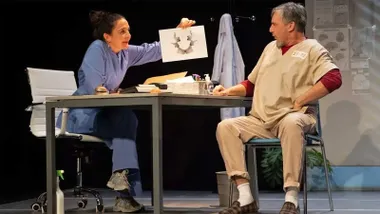 Peña y Fernández, sentados en una mesa en un momento de la obra teatral.