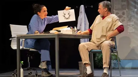 Peña y Fernández, sentados en una mesa en un momento de la obra teatral.