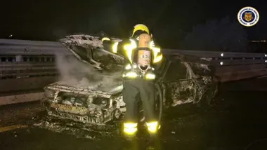 Bombero delante del coche totalmente calcinado en la noche y con la pintura quemada.