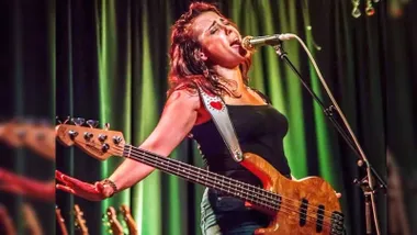 Daniel Nicole, con vestido negro, en un escenario de cortinas verdes, cantando.